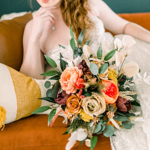 Boho bridal bouquet with rust orange roses, magenta peonies, beige ranunculus, feathers, and greenery 